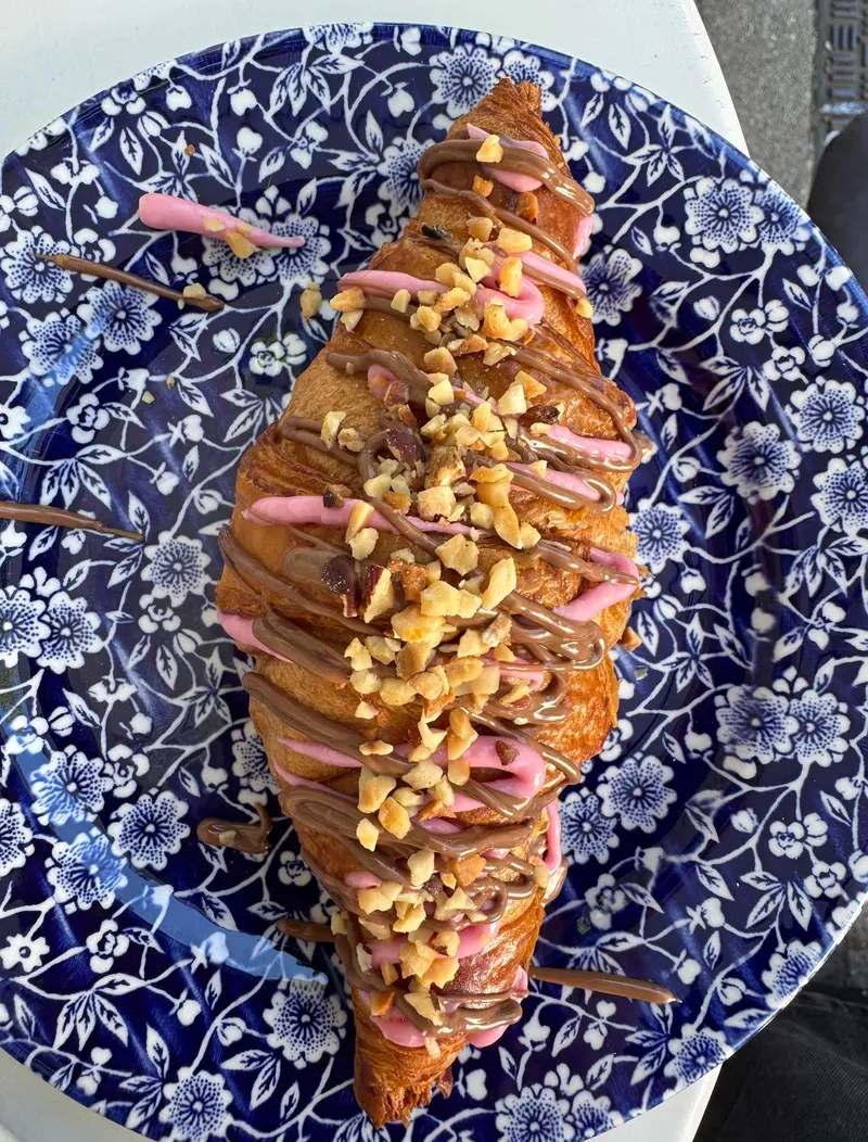 Croissant mit Nutella, rosa Glasur und gehackten Haselnüssen